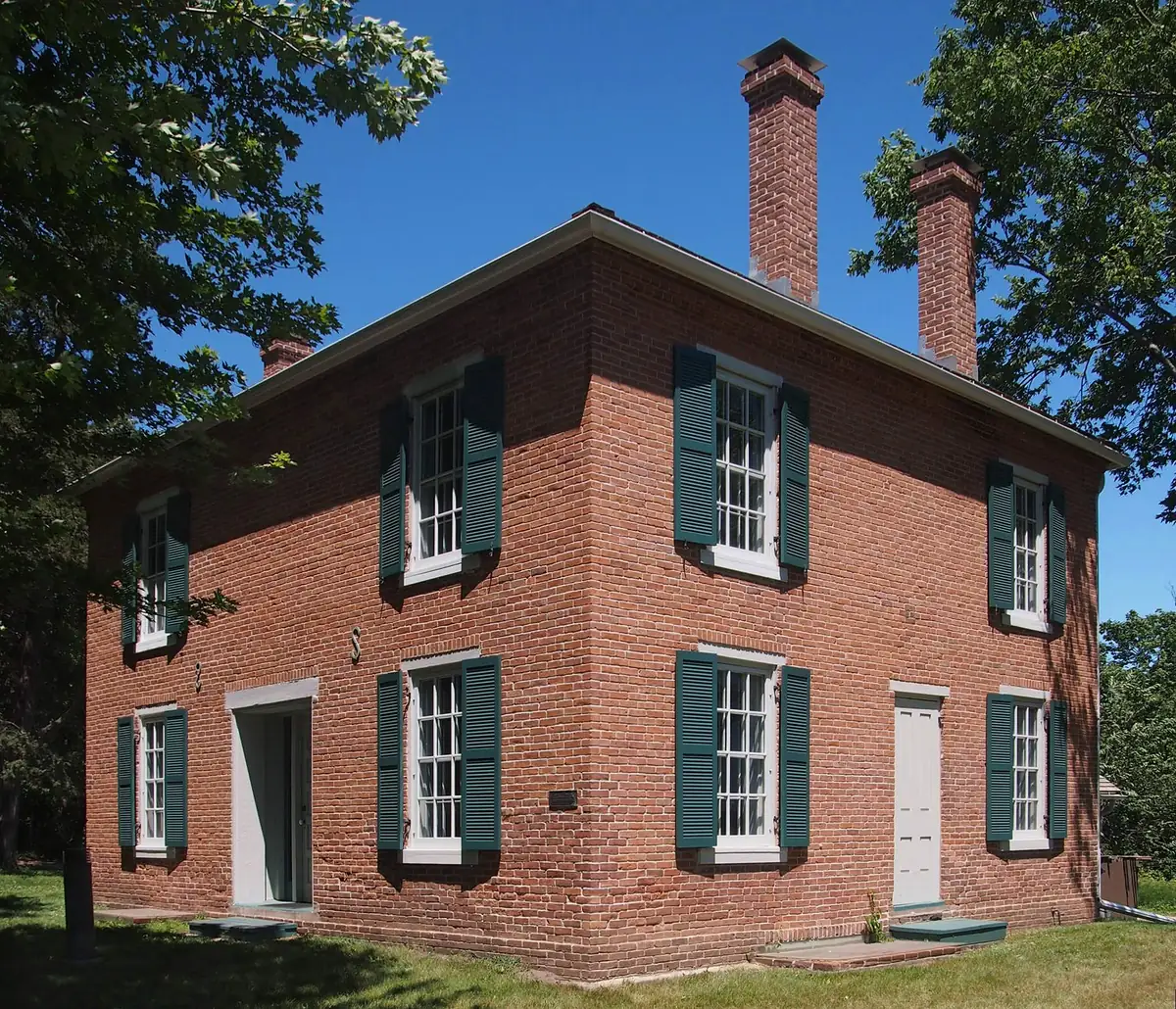 Two-story red-brick 1850s house with green shutters and twin chimneys at the Gideon H. Pond historic site in Bloomington