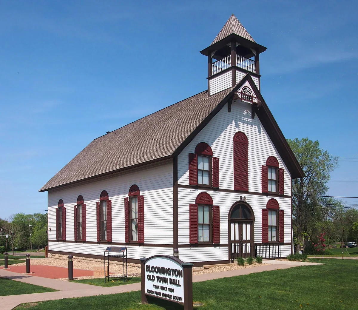 White clapboard 1892 town hall with dark-red arched shutters and a cupola on Penn Avenue South in Bloomington
