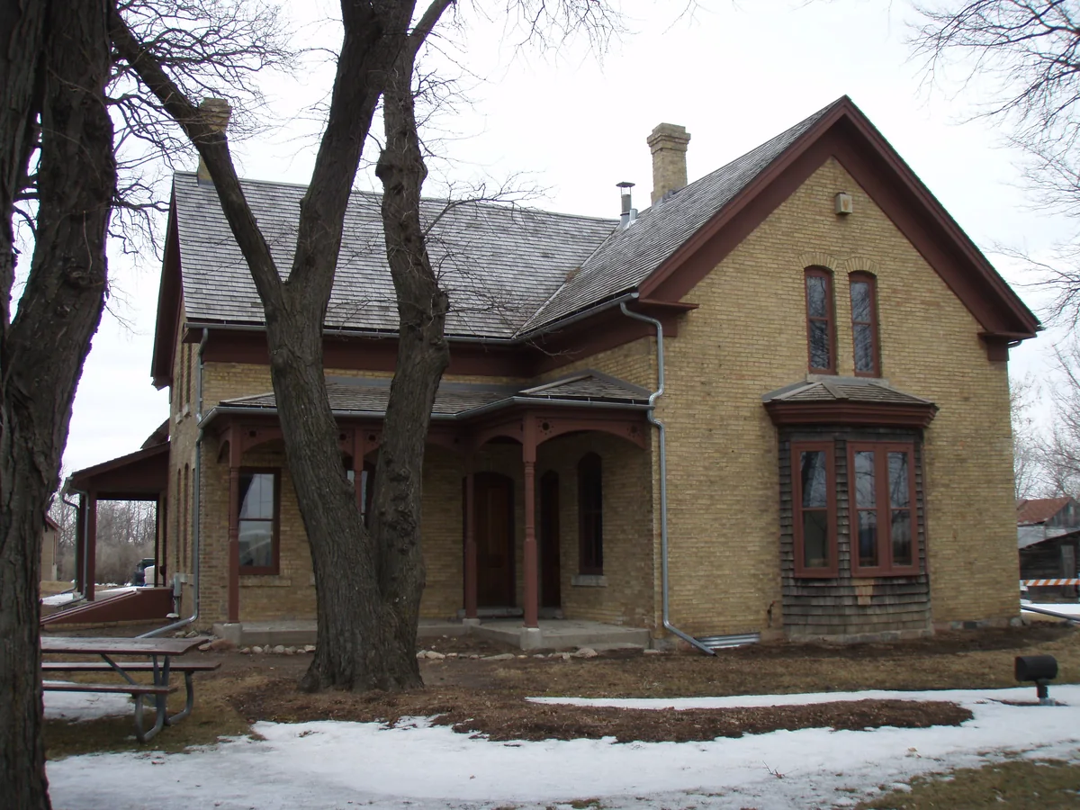 Cream-brick 1880s farmhouse with dark-red trim, a decorative front porch and a bay window at the Cummins-Grill-Phipps House in Eden Prairie