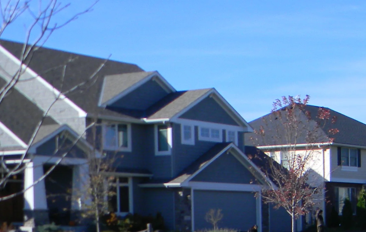 Two neighboring two-story suburban homes with gabled roofs, lap siding and attached garages beneath a blue sky in Eden Prairie