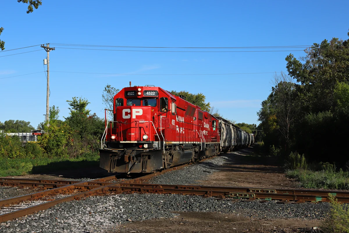 Red Canadian Pacific locomotive pulling freight cars through a tree-lined rail crossing in Golden Valley