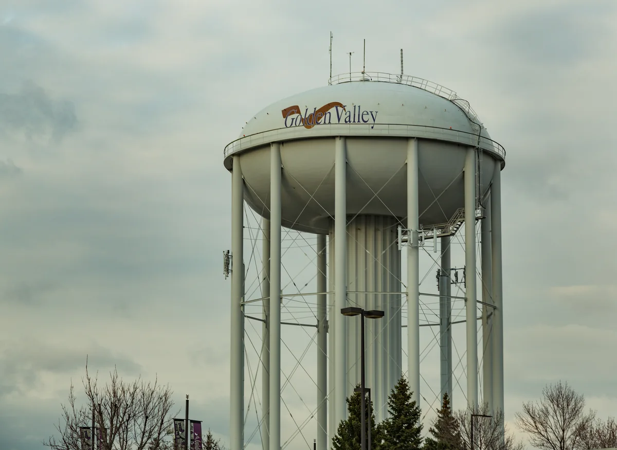Pale elevated water tank bearing the Golden Valley name above trees under an overcast sky