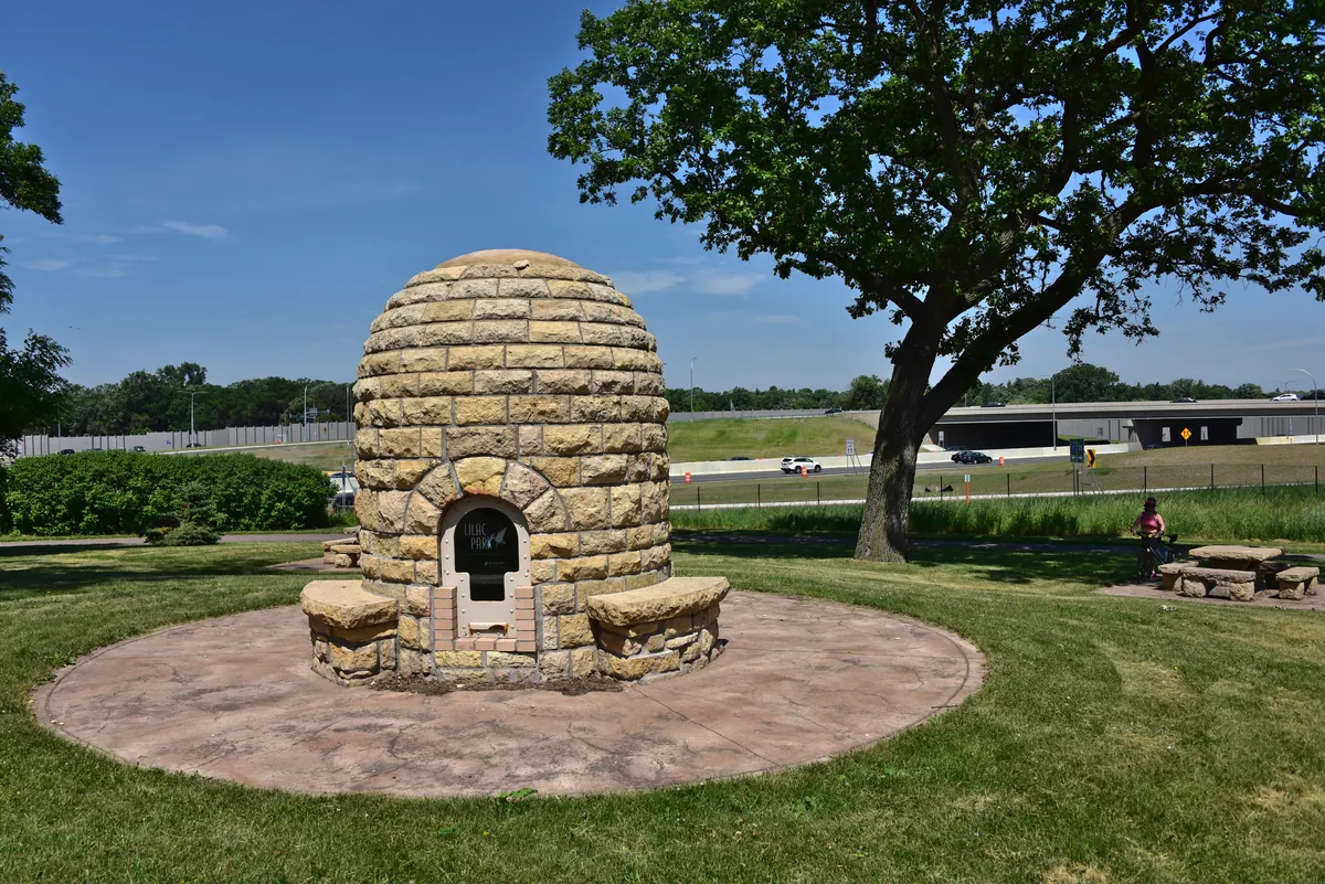 Beehive-shaped 1930s WPA stone fireplace with built-in benches under a large oak in Lilac Park, St. Louis Park
