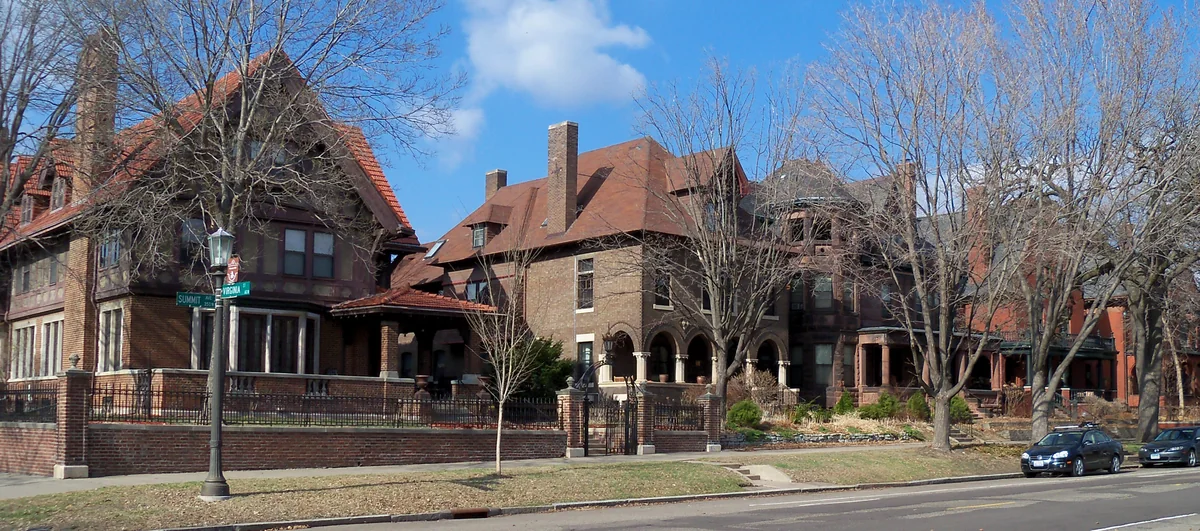 Row of large brick and stone mansions with steep tile roofs behind wrought-iron fences on Summit Avenue in St. Paul, early spring