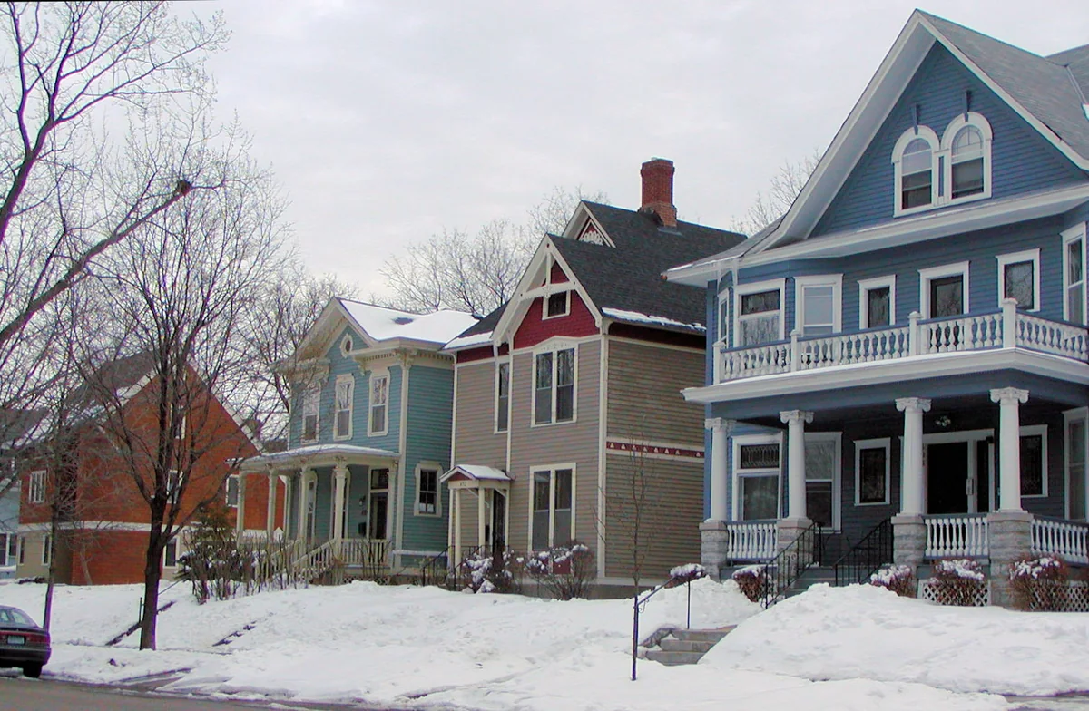 Row of painted Victorian wood-frame houses in blue, red and green with front porches and snowy yards in St. Paul's Woodland Park Historic District