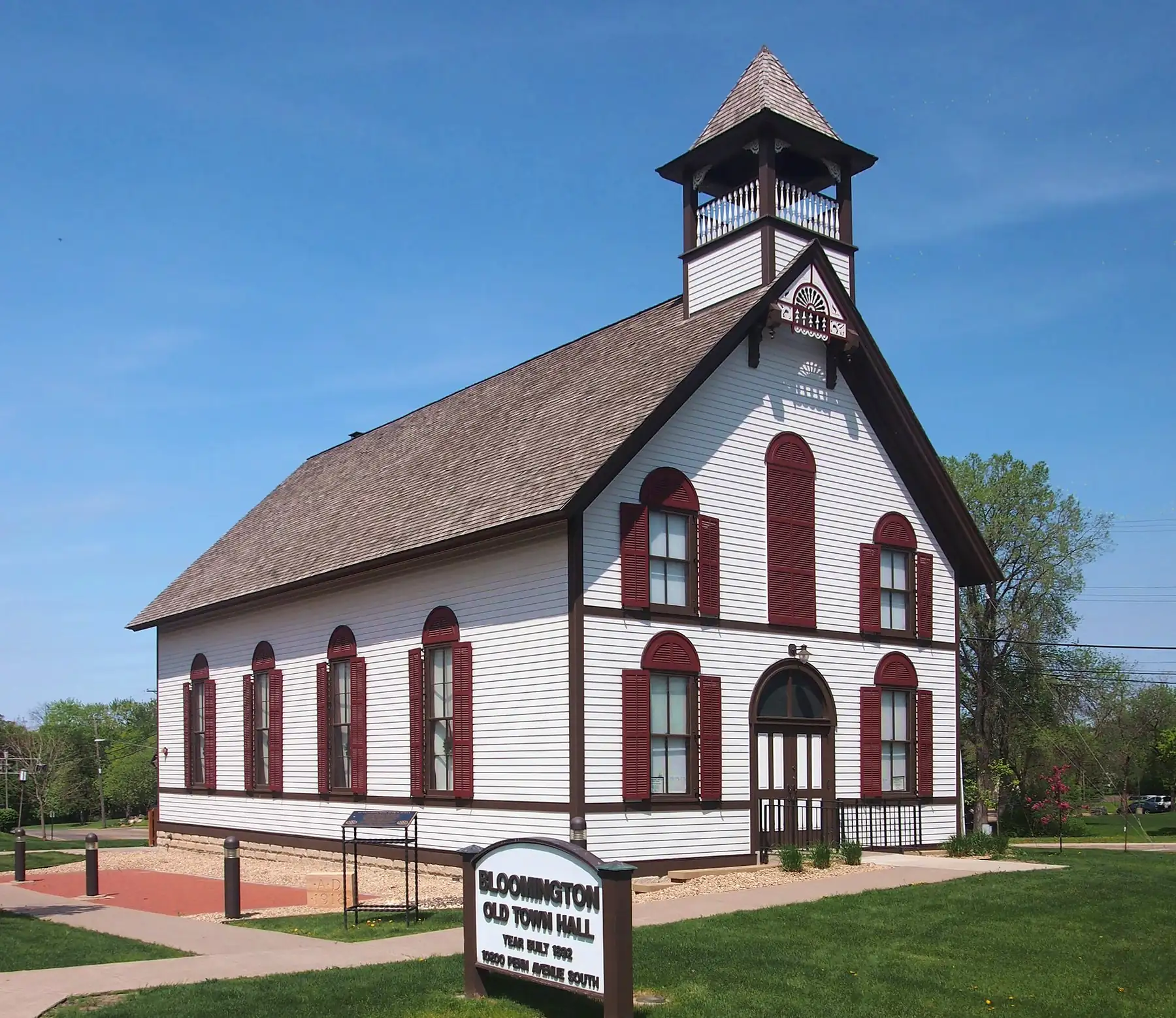White clapboard 1892 town hall with dark-red arched shutters and a cupola on Penn Avenue South in Bloomington