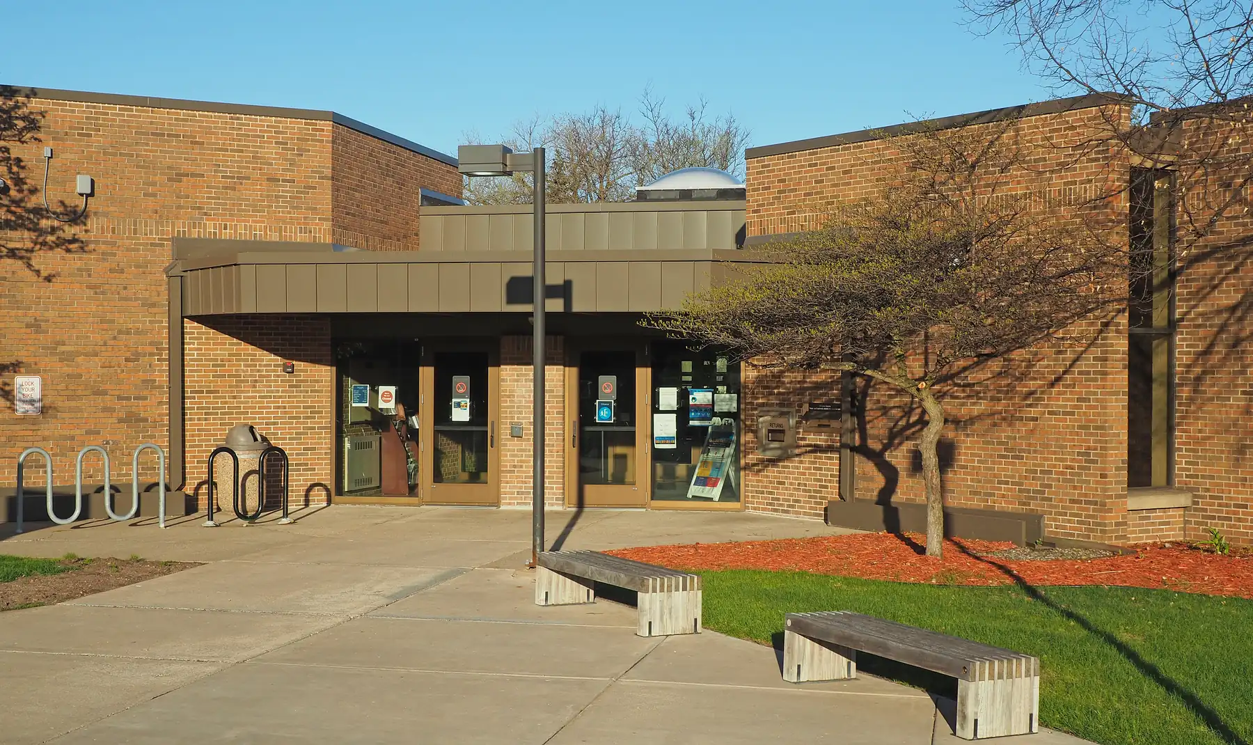 Brick Golden Valley Library entrance with bicycle racks, concrete benches and bare trees