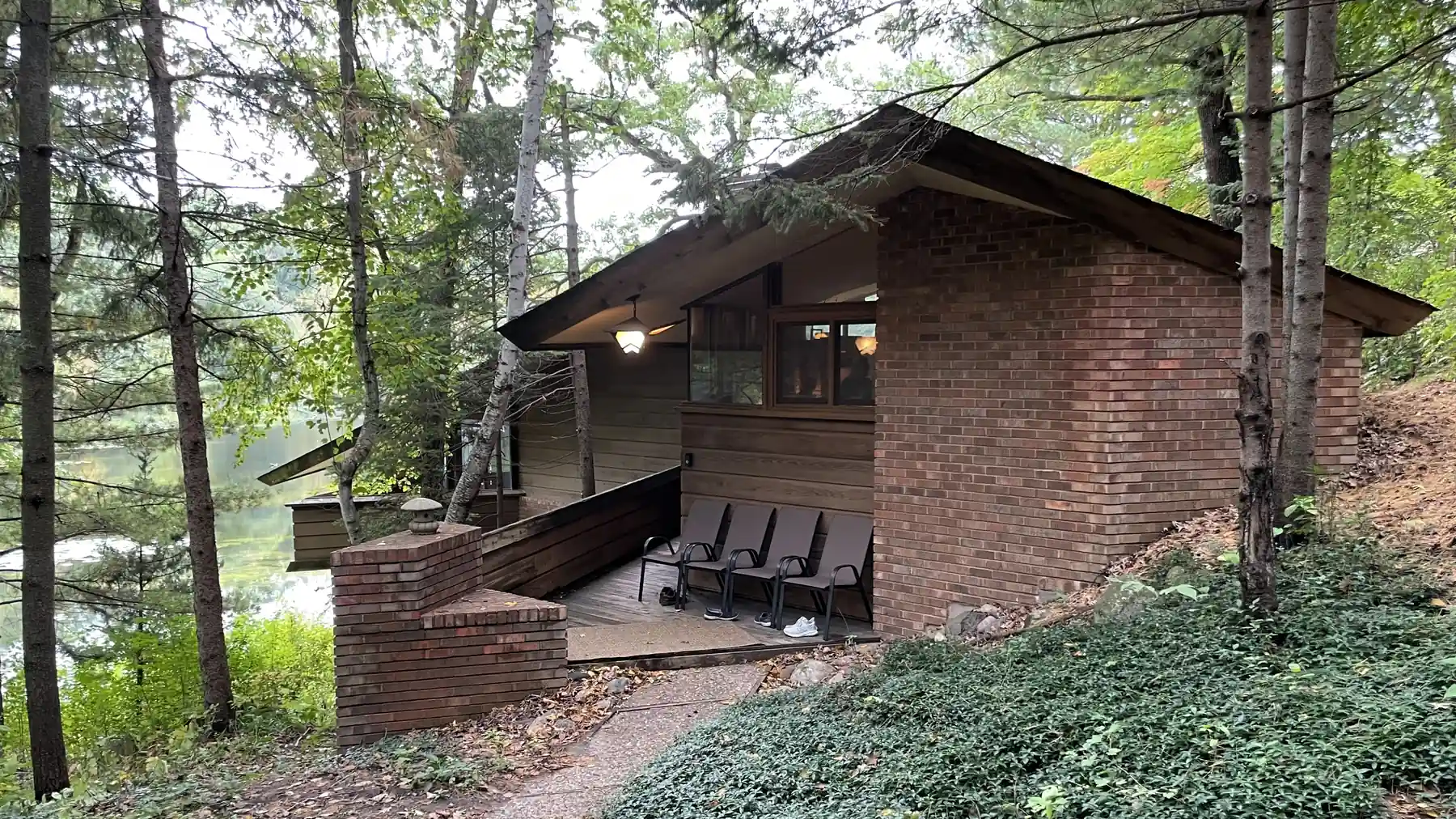 Low brick-and-cedar midcentury house with a long overhanging roof and a wooded entry walk beside a lake in Burnsville