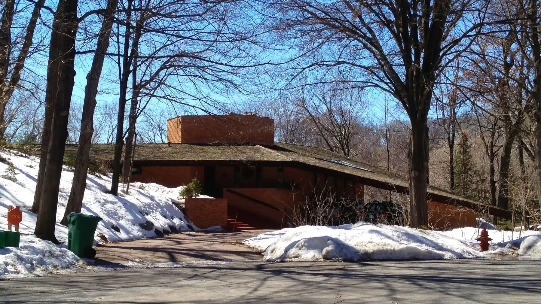 Low brick Usonian house with a broad shingled roof on a wooded, snowy hillside in St. Louis Park