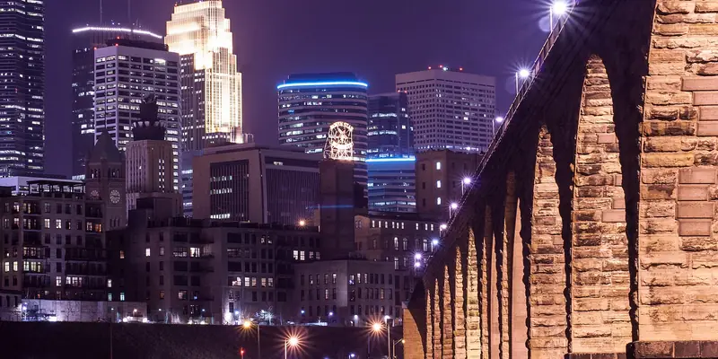 Downtown Minneapolis lit up at night, with the stone arches of the Stone Arch Bridge on the right