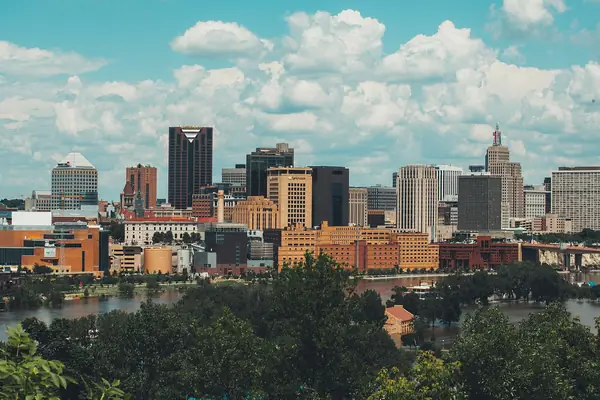 Downtown St. Paul skyline under a summer sky, with trees and river water in the foreground