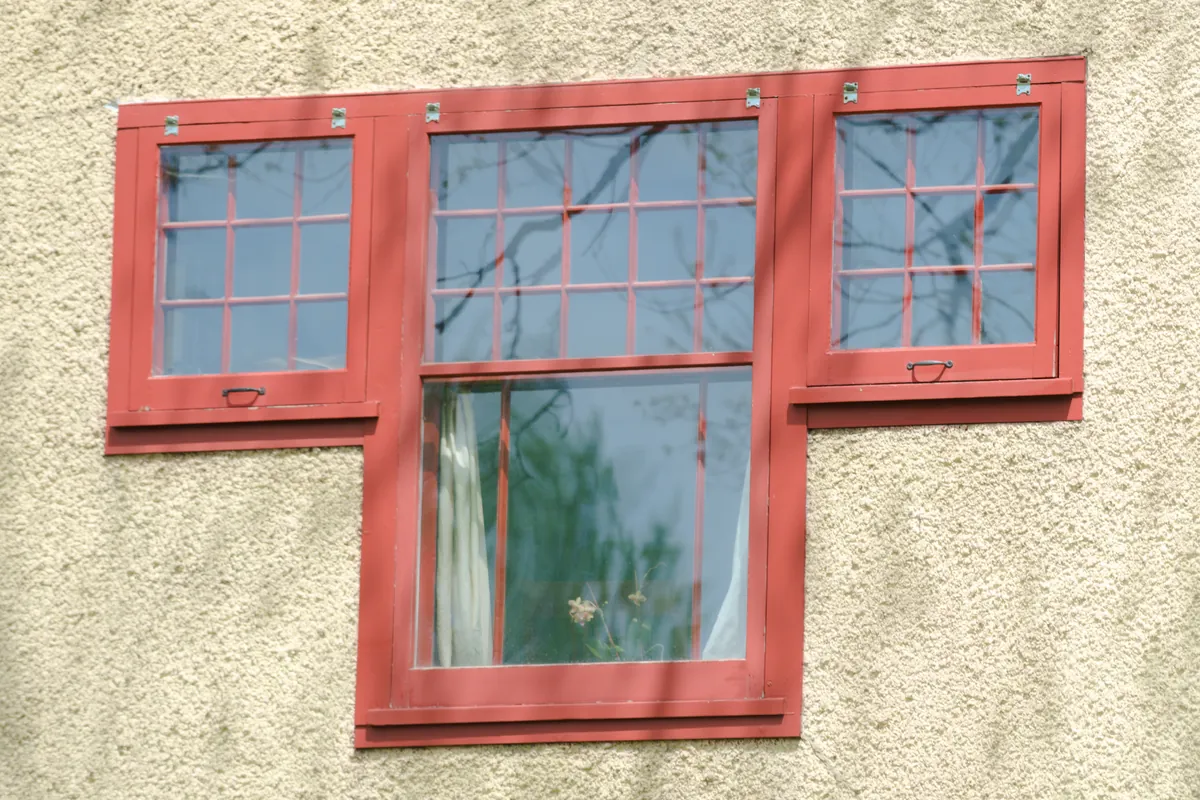 Close view of a painted wood window group on a 1910 stucco house in Minneapolis, with red divided-light sash, casings and sills set in a tan stucco wall