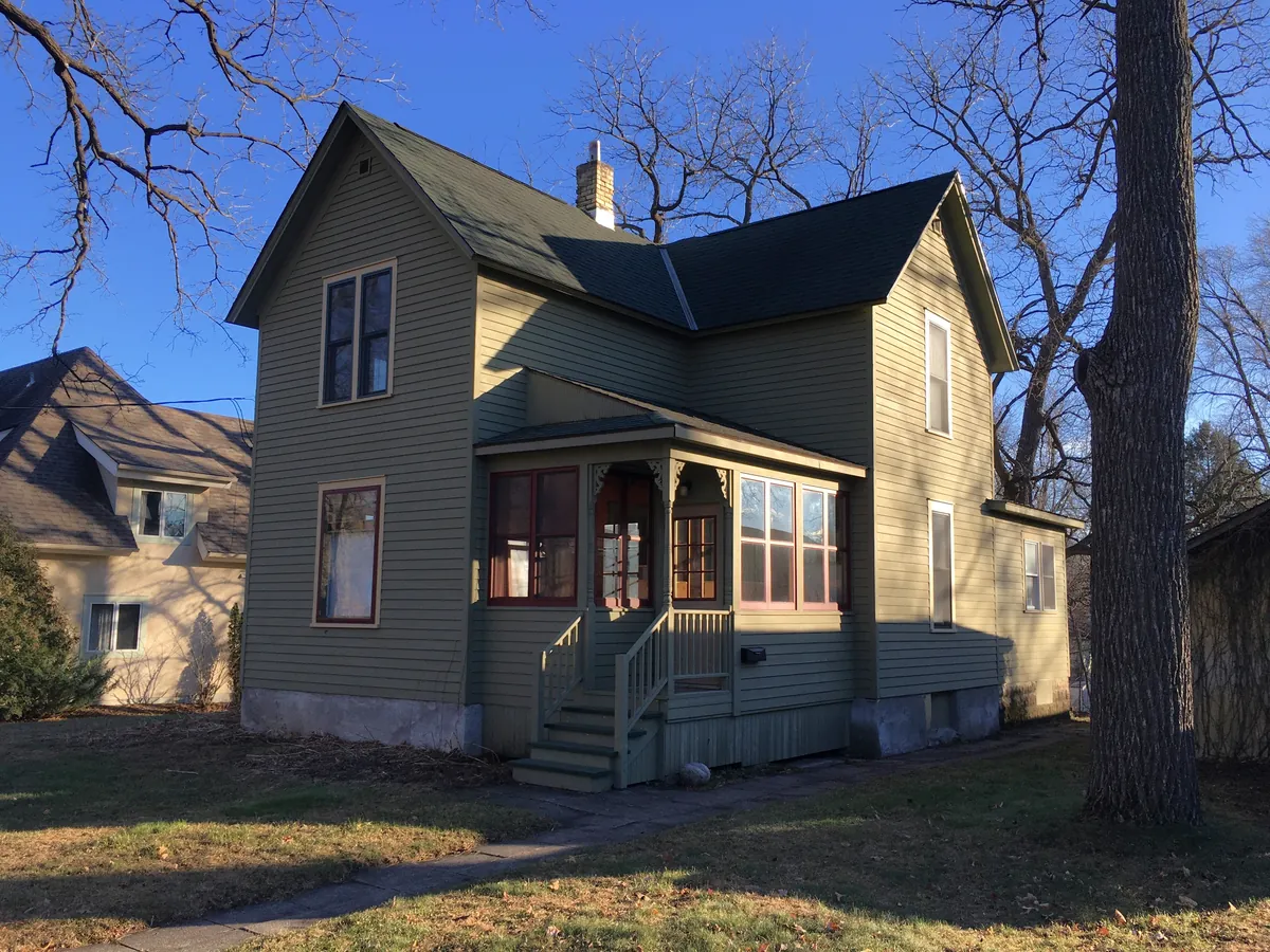 A green lap-sided Queen Anne house in Northfield, Minnesota, in low autumn sun, with the porch and back wall in shade