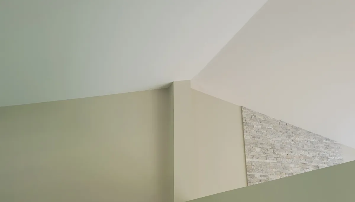 Freshly painted walls and an angled ceiling meeting at crisp, even lines, with a stone accent wall beyond