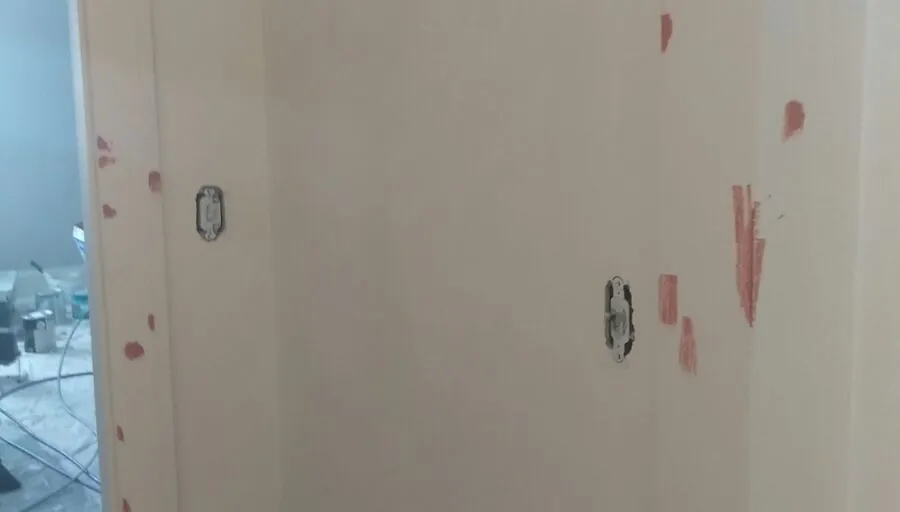 Small dabs of pink spackle over nail holes on a white wall and door casing, drying before sanding