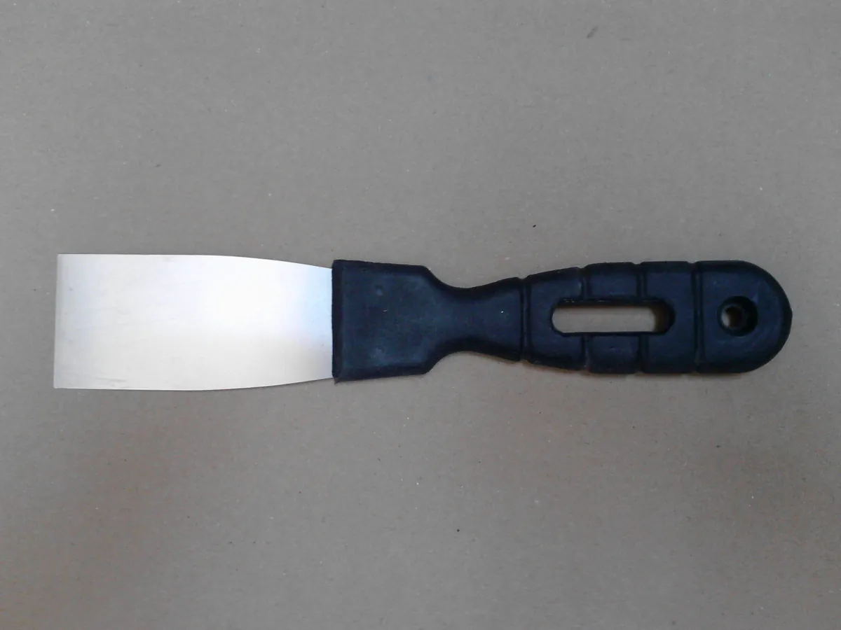 A clean steel putty knife with a black handle lying on brown kraft paper