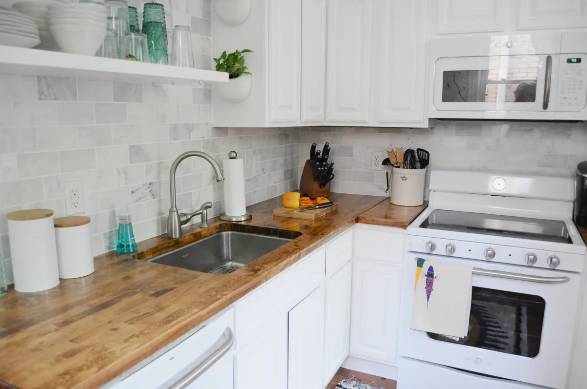 Kitchen with white painted raised panel cabinets, butcher block countertops, an undermount stainless sink with a brushed nickel faucet, marble subway tile backsplash and a white range